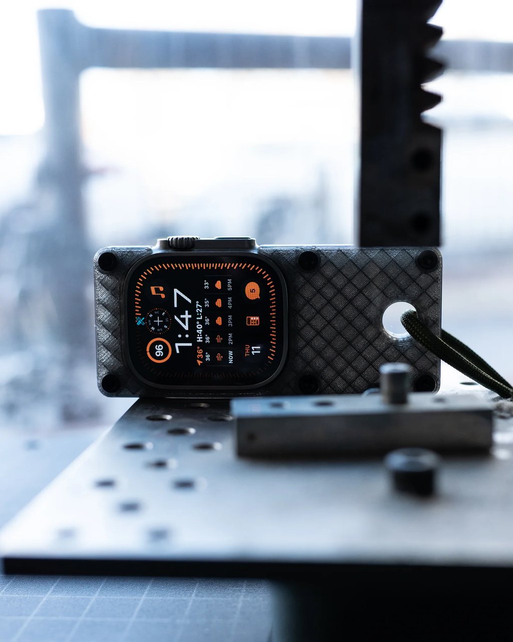The case standing on a workbench by a window, watch face showing the time and weather